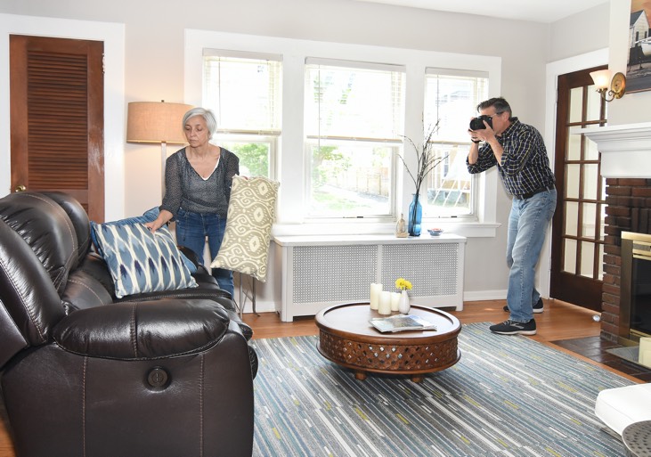 Man taking a photo of a woman putting pillows on a couch