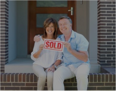 Couple sitting on front porch holding a sold sign